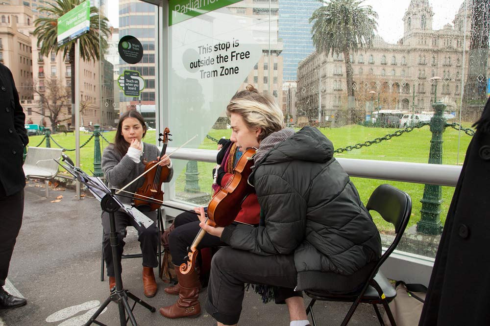 Violinists sitting at a tram stop near Parliament station
