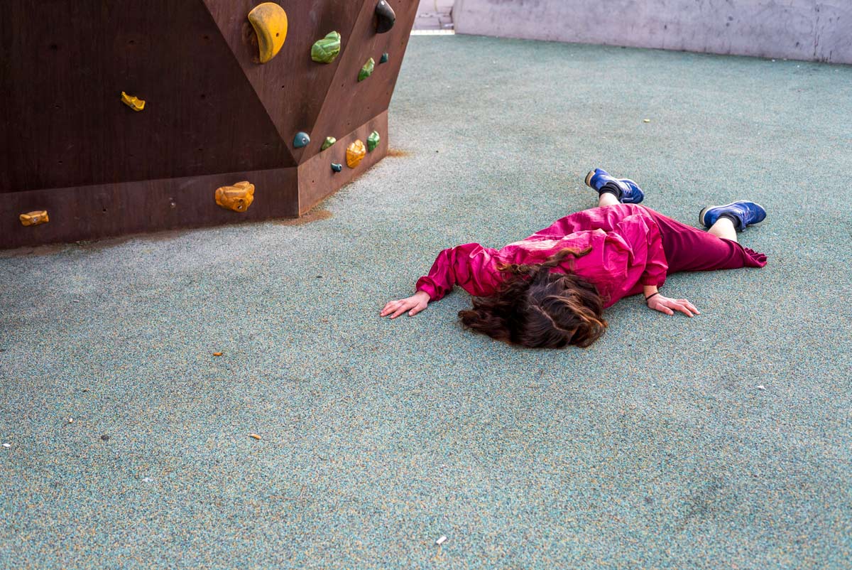 A person lying on the ground, next to a rock climing structure.