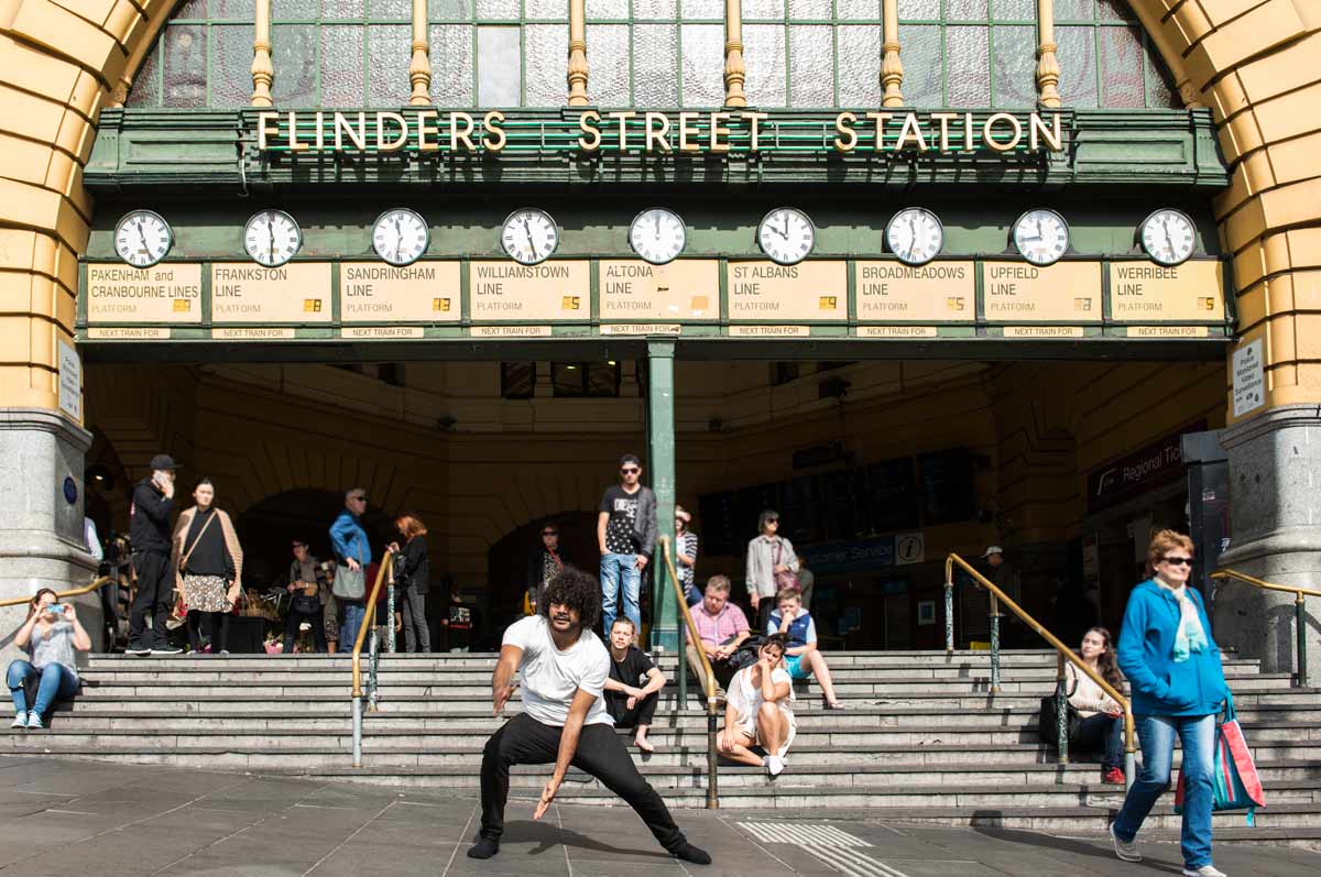 A man dancing in front of the Flinders Street Station entrance. Bystanders are watching and taking photos.