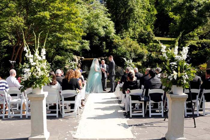 Wedding scene in park setting with bride and groom at end of aisle and small group of guests seated on either side