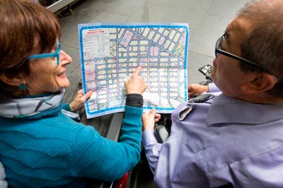 Two people who are both in wheelchairs looking at a mobility map of Melbourne city